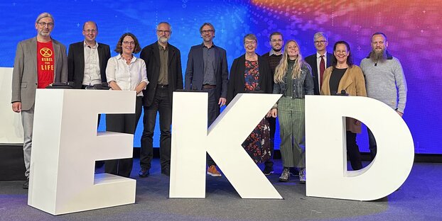 Die Mitwirkenden am Themenkomplex Klimaschutz stehen vor den großen weißen Buchstaben EKD