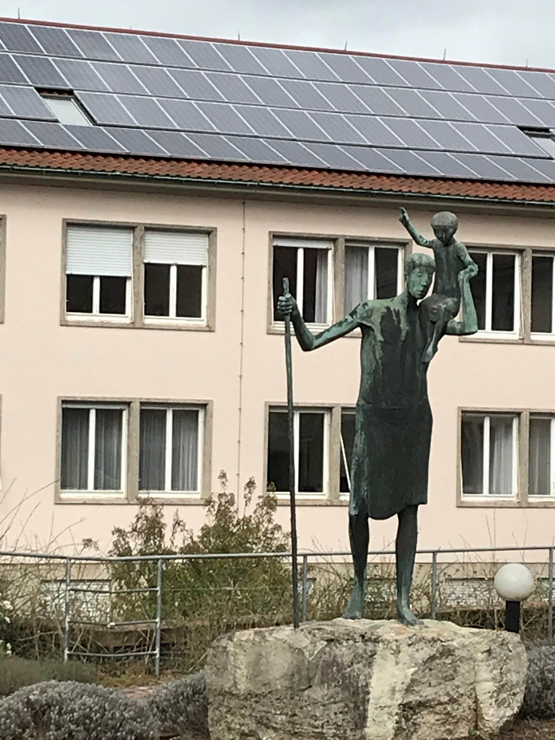 Christophorus-Skulptur vor einem kirchlichen Gebäude mit Photovoltaik auf dem Dach